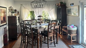 A dining area with a wooden table and chairs, a chandelier, and a view of the outdoors through sheer curtains. - Relax villa ,hot tub and New Heated  pool ,7 minutos from the beach  (Hampton Bays)