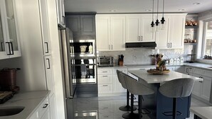 A modern kitchen with white cabinetry, a marble floor, and a central island with bar stools. - Relax villa ,hot tub and New Heated  pool ,7 minutos from the beach  (Hampton Bays)
