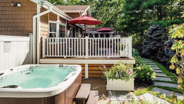 A hot tub, a covered patio with a railing, and a garden with flowers and a rock. - Relax villa ,hot tub and New Heated  pool ,7 minutos from the beach  (Hampton Bays)
