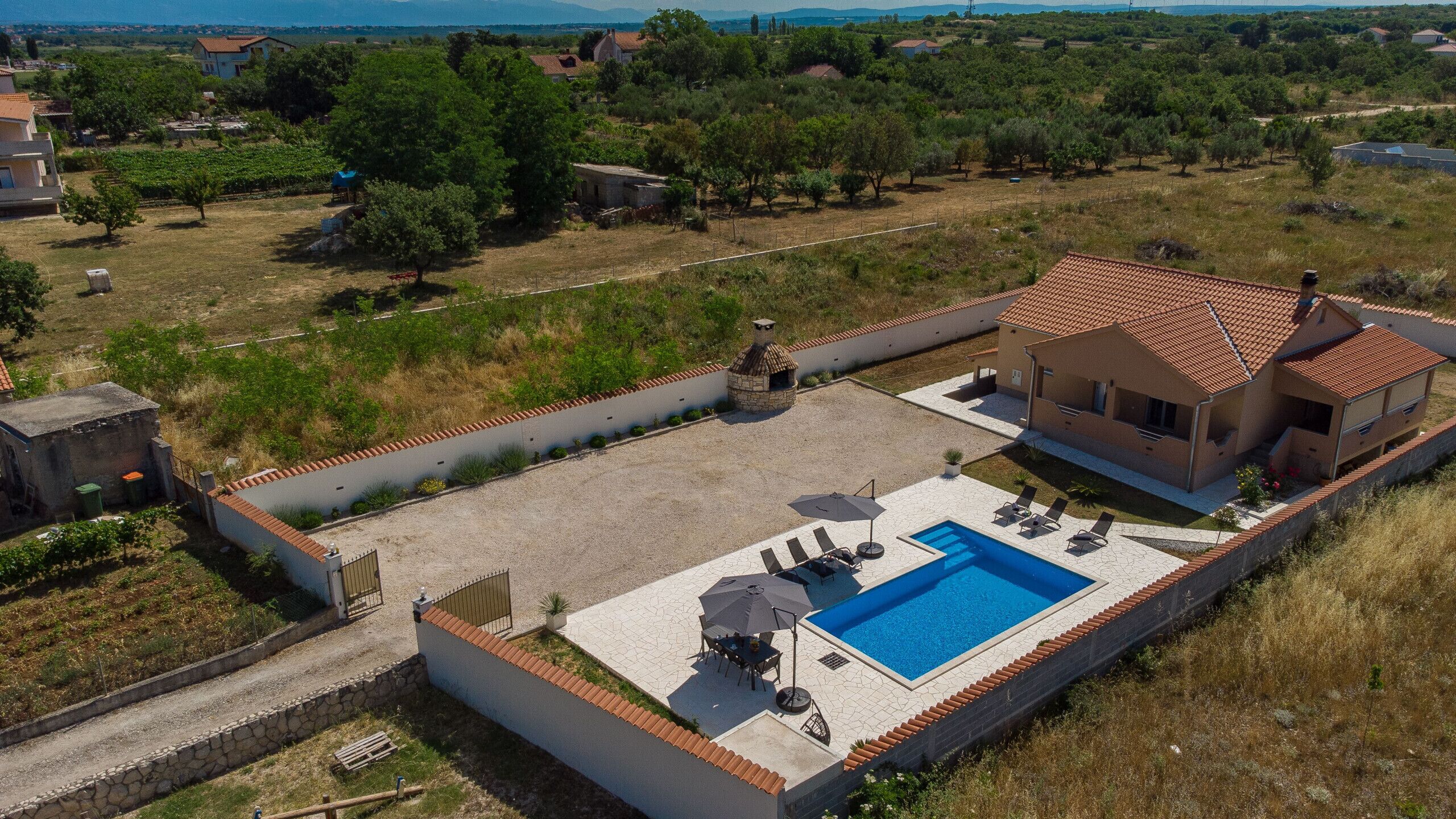 A residential property with a swimming pool, outdoor seating, and a stone oven.