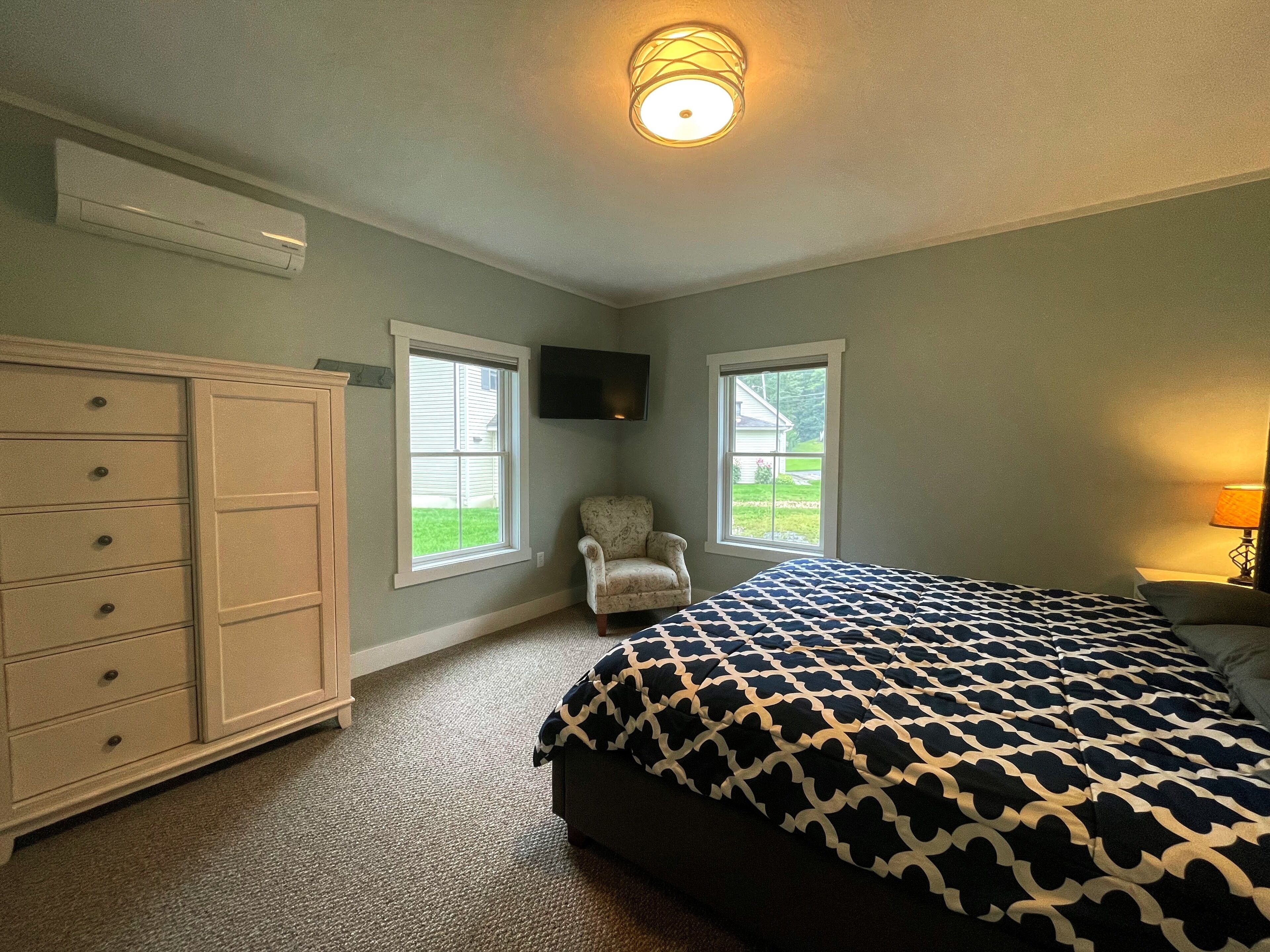 Quarto com cama, penteadeira, cadeira e duas janelas.