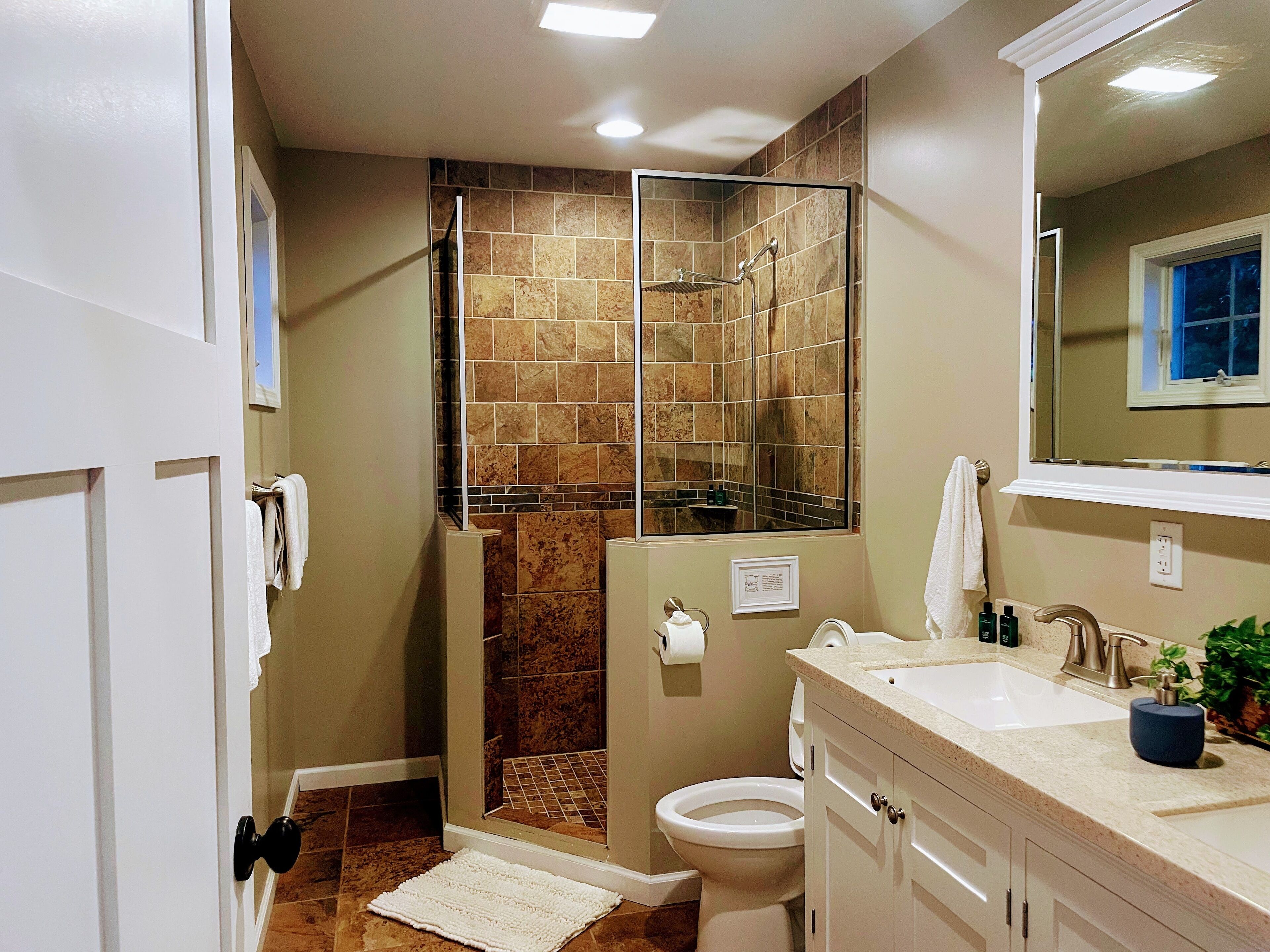 A bathroom with a shower, toilet, sink, and a mirror.