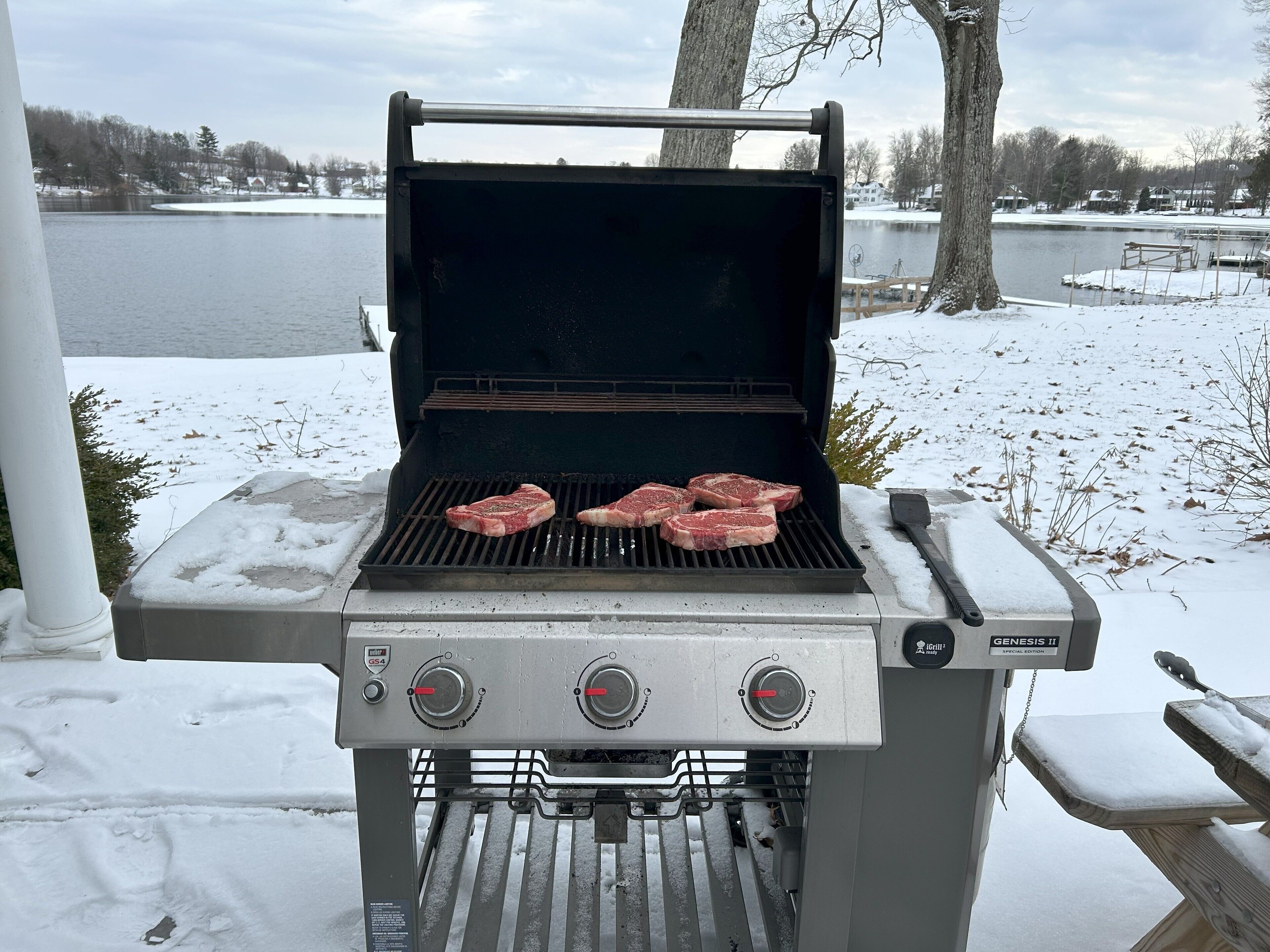 Ein Genesis II tragbarer Grill mit vier Steaks, die draußen zubereitet werden.
