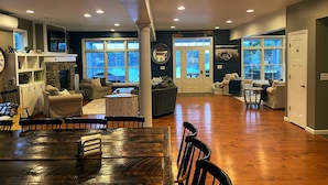 A spacious living area with a fireplace, large windows, and a dining table with chairs.