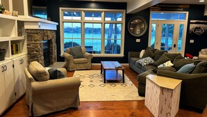 A living room with a stone fireplace, large windows, and a view of a body of water.