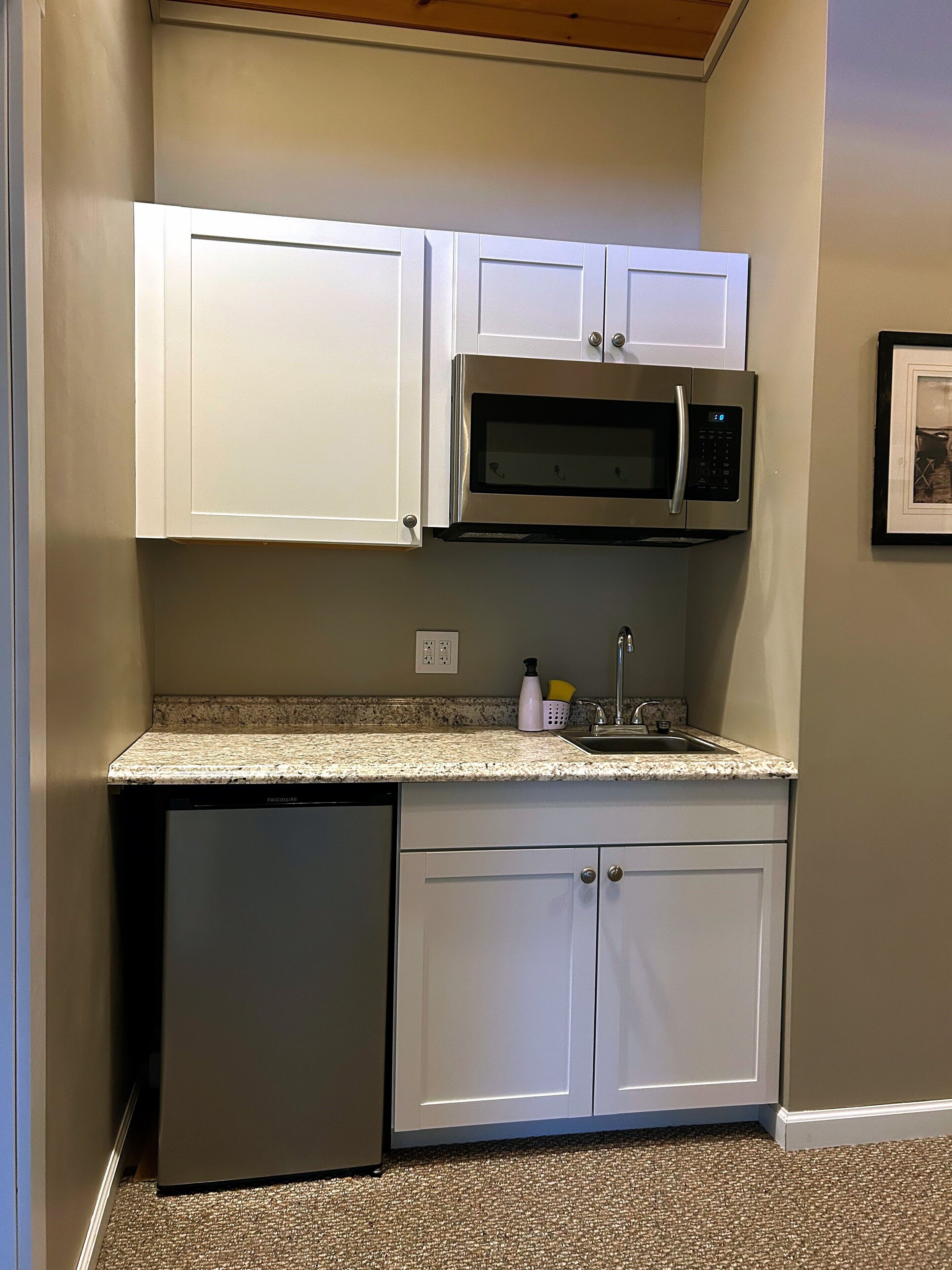 A compact kitchen with white cabinets, a stainless steel microwave, and a dishwasher.