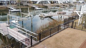 A marina with docks and boats, surrounded by a wooden deck and a metal fence. - ABSOLUTIKI - 3 min walk to beach, Canal with Boat Dock, Outdoor Bar & Shower (Ocean Isle Beach)
