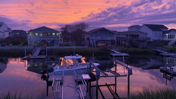 A waterfront property with docked boats, a pier, and houses with balconies overlooking the water. - ABSOLUTIKI - 3 min walk to beach, Canal with Boat Dock, Outdoor Bar & Shower (Ocean Isle Beach)