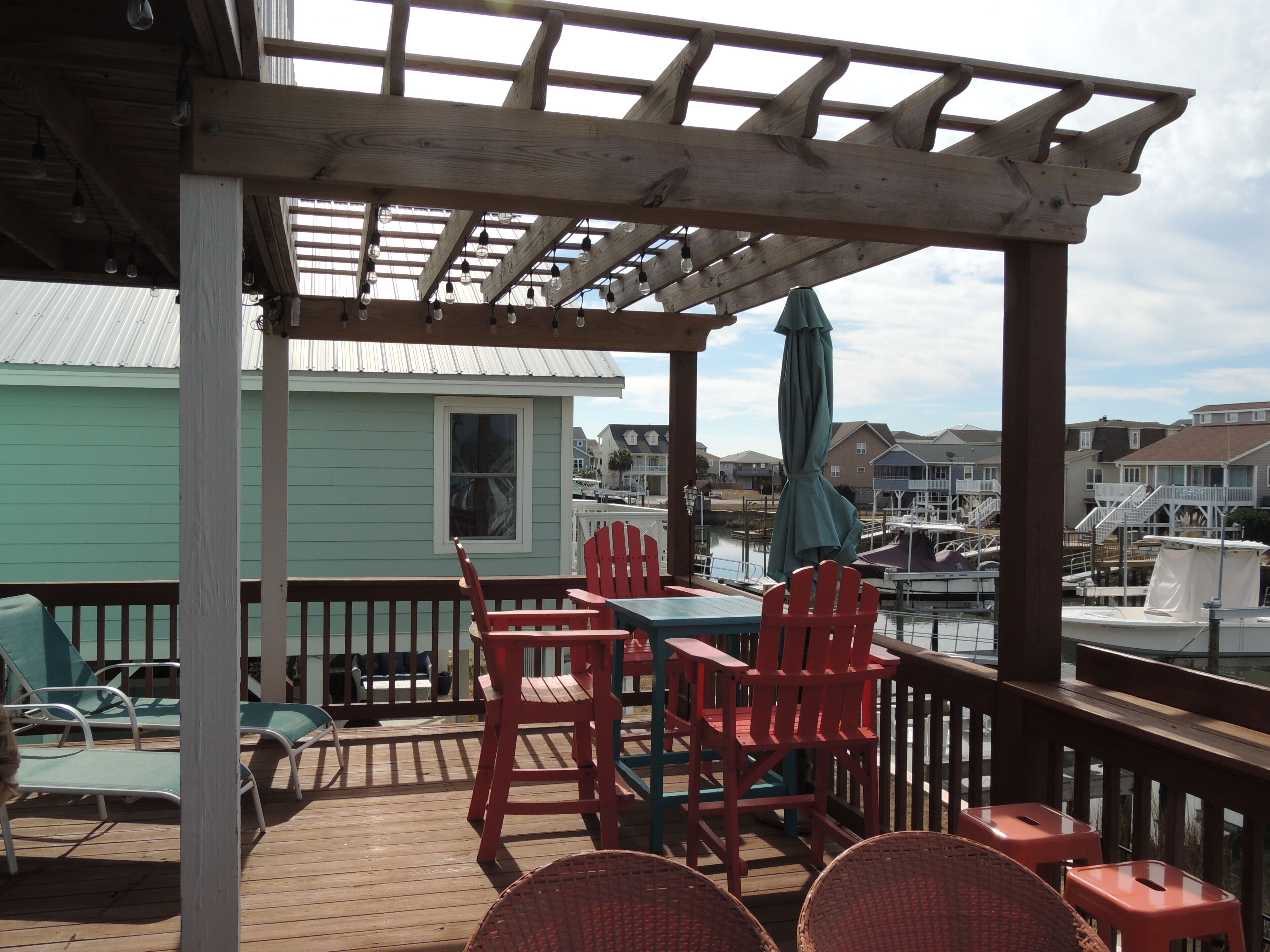 A wooden deck with a table and chairs, overlooking a marina with boats.
