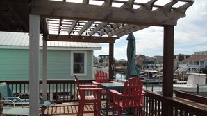 A wooden deck with a table and chairs, overlooking a marina with boats. - ABSOLUTIKI - 3 min walk to beach, Canal with Boat Dock, Outdoor Bar & Shower (Ocean Isle Beach)