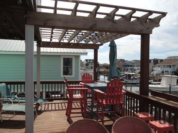 A wooden deck with a table and chairs, overlooking a marina with boats.