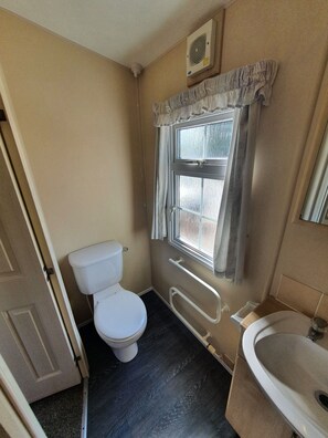 Un baño pequeño con inodoro, una ventana con cortinas, un pasamanos y un lavabo.