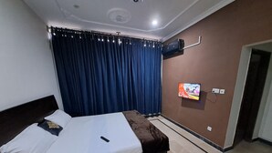 Ein Hotelzimmer mit Bett, Vorhängen, einem an der Wand befestigten Fernseher und einem Fliesenboden.