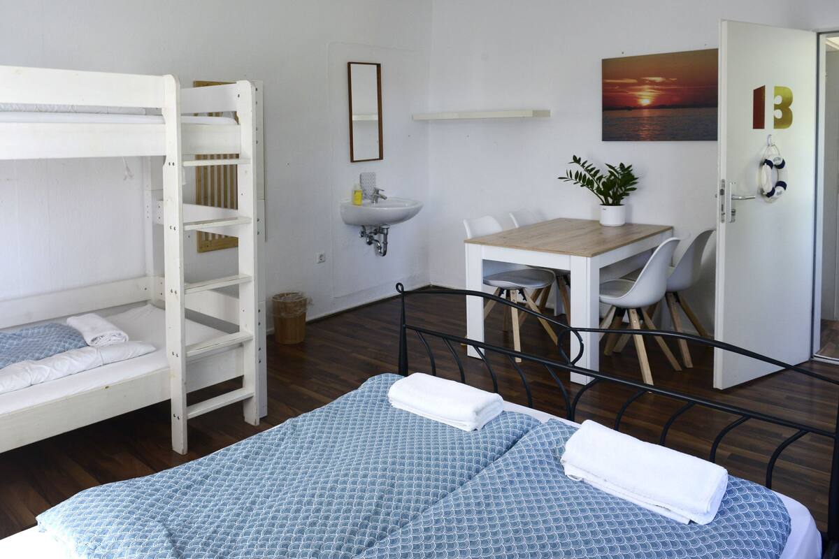 A room with bunk beds, a small table with chairs, a sink, and a potted plant.
