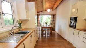 Cozinha moderna com piso de madeira, área de refeições com mesa e cadeiras, e vista para o verde lá fora.