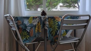 Une pièce avec une table et des chaises près d’une fenêtre, une décoration en forme de pomme de pin, et une vue sur des arbres et un bâtiment à l’extérieur.