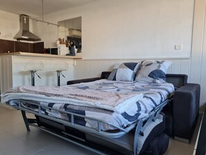 A modern bedroom with a bed, bedside tables, and a small kitchenette area.
