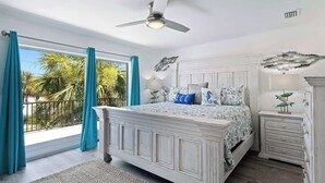 A bedroom with a bed, bedside tables, a ceiling fan, and a view of the outdoors.