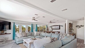 A spacious living room with a light blue sectional sofa, a flat-screen TV, and a ceiling fan.