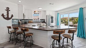 A modern kitchen with a central island, bar stools, and a view to a balcony.