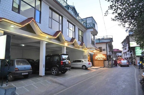 A hotel with a covered parking area, multiple cars parked, and a sign indicating a restaurant. - Hotel Hemkunth (Kasauli)