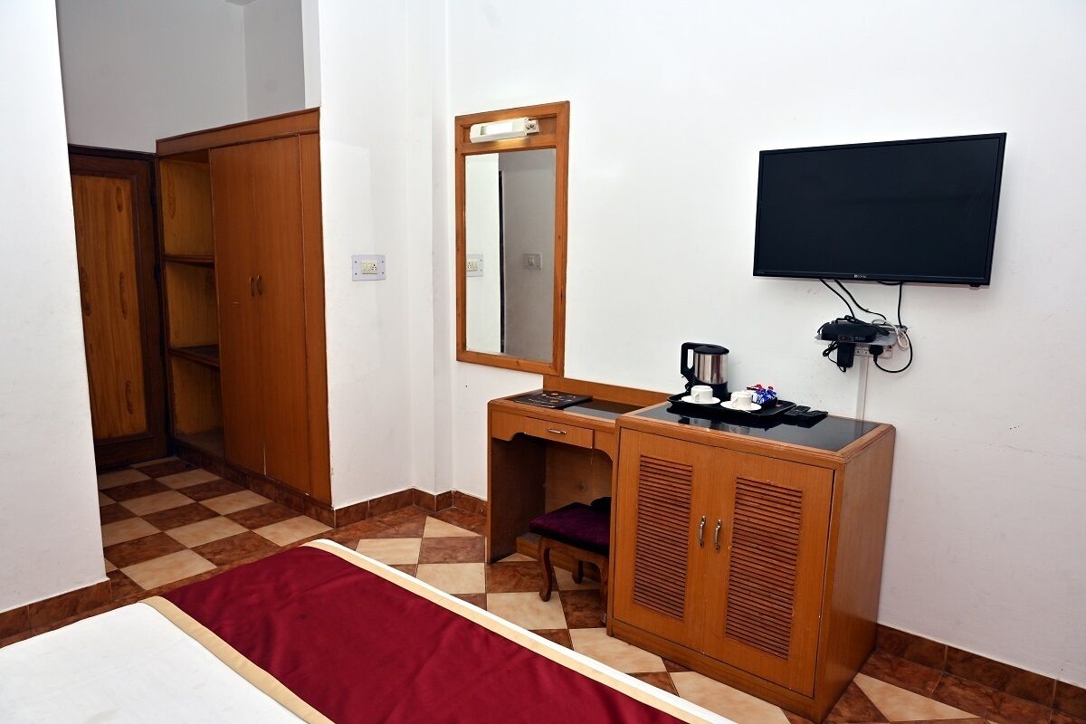 A bedroom with a bed, a wooden desk, a mirror, a television, and a wardrobe.
