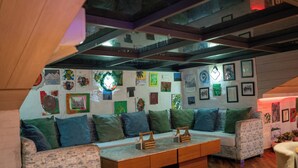 A cozy living room with a sofa, cushions, a coffee table, and a wall adorned with various framed artworks. - Hotel Hemkunth (Kasauli)