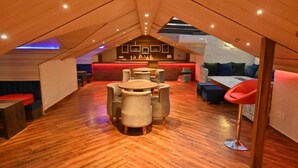 A cozy attic space with a wooden floor, a central round table, and a bar area with stools. - Hotel Hemkunth (Kasauli)