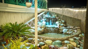 A small, illuminated water feature surrounded by rocks and potted plants in an outdoor setting. - Hotel Hemkunth (Kasauli)