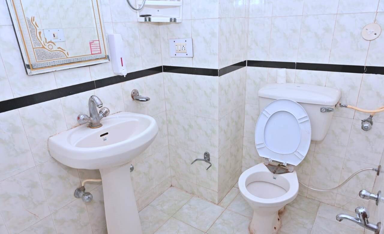Un baño con lavamanos pedestal, inodoro y espejo con marco decorativo.