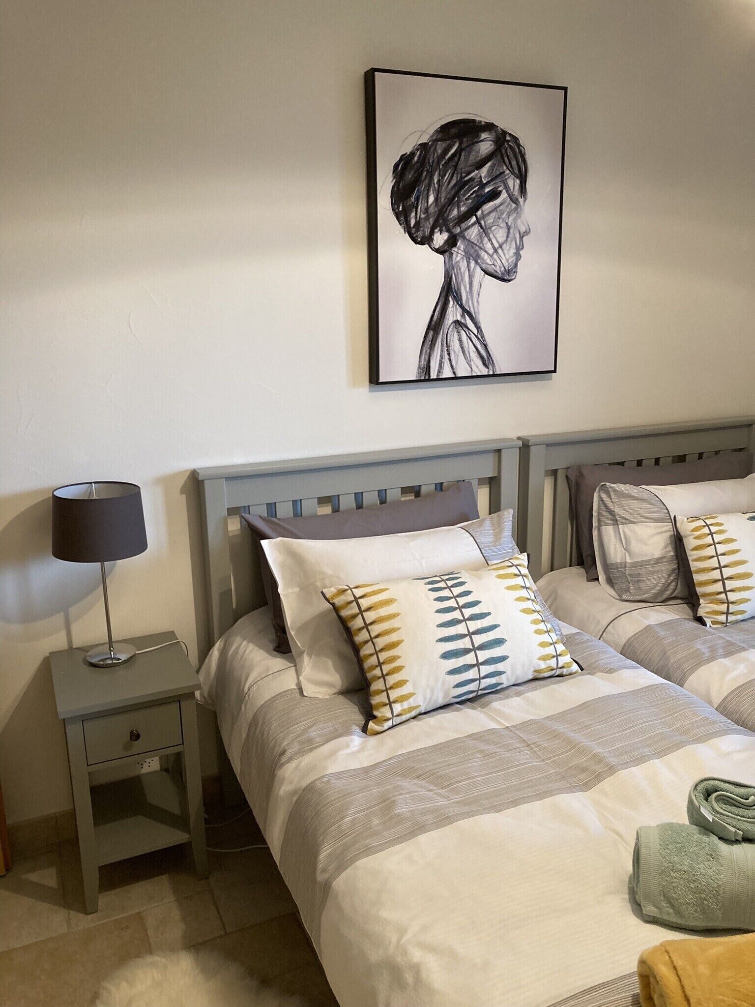 Quarto com duas camas, uma mesa de cabeceira com abajur e uma obra de arte emoldurada na parede.