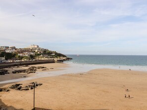A beach with a rocky shoreline, a pier, and buildings on a hill in the background. - 6 Ocean Heights (Newquay)