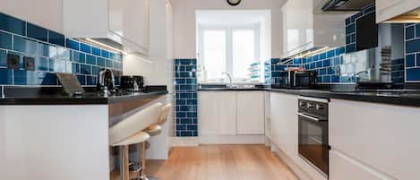 A modern kitchen with white cabinets, blue tiles, stainless steel appliances, and a wooden floor.