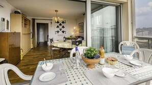 Un comedor con una mesa dispuesta para cuatro personas, vistas de la ciudad a través de amplios ventanales y una cocina al fondo.