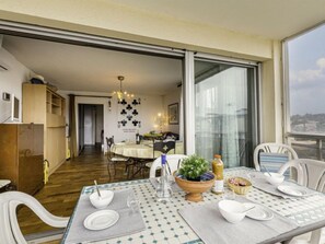 A dining area with a table set for four, a view of the city through large windows, and a kitchen in the background.