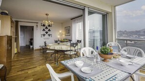 Un comedor con una mesa dispuesta para cuatro personas, una araña y vistas de la ciudad a través de amplios ventanales.