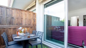 A patio with a table set for four, surrounded by chairs, and a large sliding glass door leading to an interior space.