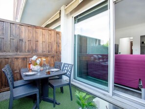 Pátio com mesa posta para quatro pessoas, rodeado de cadeiras, e uma grande porta de vidro deslizante que dá para um espaço interno.