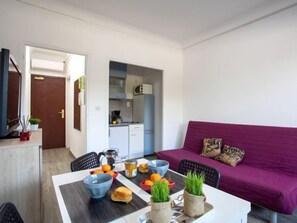 Een compacte leefruimte met een eethoek, kitchenette en een paarse bank.