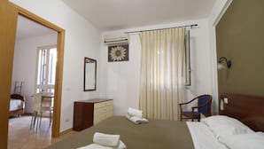Une chambre d’hôtel avec un lit, un bureau, une chaise, un miroir et une fenêtre avec des rideaux.
