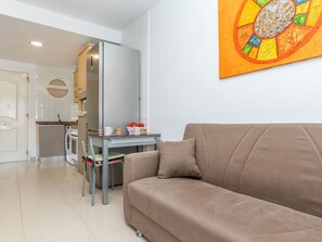 A living room with a sofa, a glass table, and a kitchen in the background.