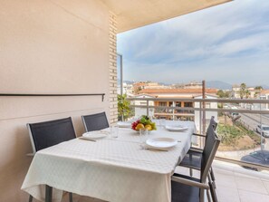 A balcony with a table set for two, a view of buildings, and a clear sky.