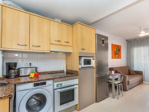 A compact kitchen with a washing machine, oven, microwave, and refrigerator.