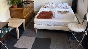 Ein kleiner, gemütlicher Raum mit einem Bett, einem Schreibtisch, einem Stuhl, einer Kommode und einer Topfpflanze.