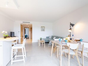 Un appartement moderne et bien éclairé, comprenant un coin repas, un salon avec un canapé et un espace cuisine.