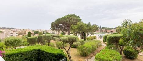 Ein Garten mit verschiedenen Bäumen und Sträuchern, einem eingezäunten Bereich und Gebäuden im Hintergrund.