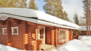Una baita di legno con tetto innevato, finestre in legno e veranda in legno.