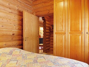 A log cabin room with a bed, wooden walls, and a door leading to another room.