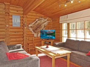 A log cabin interior with a television, a couch, a table, and a large window.