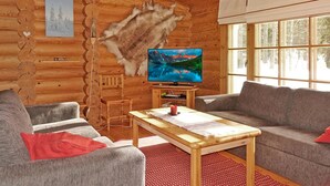 Interno di una baita di legno con televisione, due divani, un tavolino in legno e un'ampia finestra.